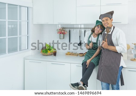 Attractive young asian couple cook burger together in white kitchen
