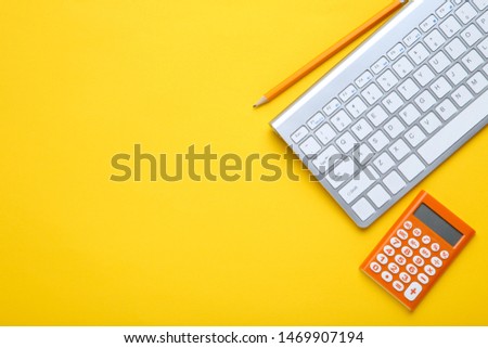 Computer keyboard with calculator and pencil on yellow background