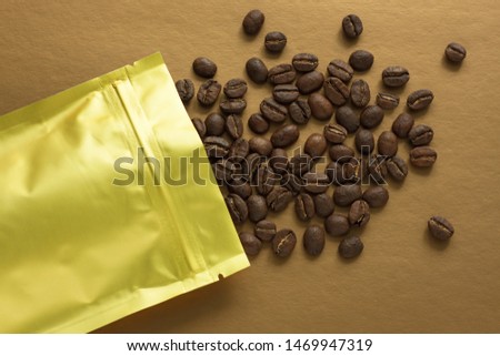 Gold foil bag with coffee beans on trend golden background. Packaging template mockup. Aluminium package for tea leaves and products. Flatlay, top view, copy space.