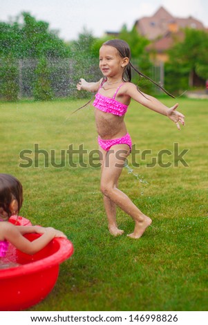 Adorable little girl in a swimsuit playing and splashing in the yard