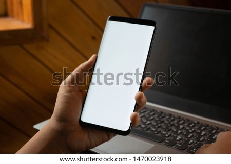 Mockup mobile phone image. Close up hands using modern smart phone Technology with blurred laptop background. Mobile phone with blank screen for your advertisement artwork.