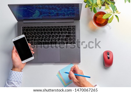 Male hands working on a laptop. Office workplace on a white table. In men's hands a mobile phone. The view from the top.
