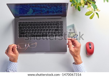 Male hands working on a laptop. Office workplace on a white table. In male hands glasses. The view from the top.