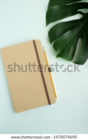 closed notebook mock ap and green leaf monstera top view on blue background. copy space