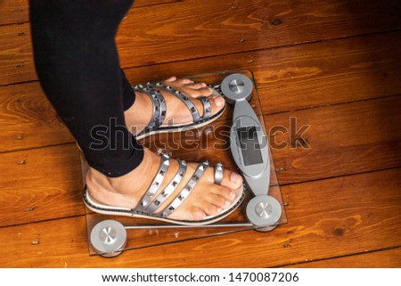 Close up of a women wearing sandals standing on top of a weighing scale