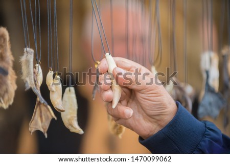 A man's hand holds a magic amulet from the tooth of an animal, different amulets hang on the laces on the stand at the fair.