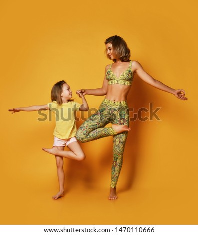 Young mother and 5-year-old daughter doing yoga exercises Pilates pose standing mountain Tadasana, hands in namaste on a yellow studio background.