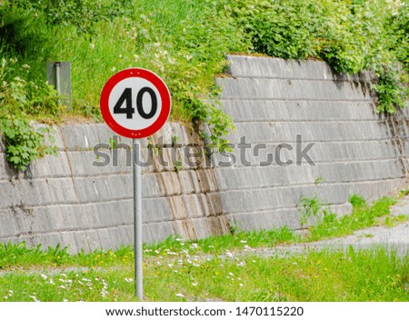 Road speed limit sign 40 in the street on background of bricks wall and greenery