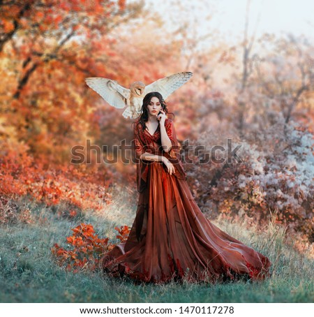pretty young girl with black hair in cold forest, orange foliage of trees, fairy of autumn season in long red burgundy vintage dress with chic train, lady with white owl on shoulder, bloody sorceress