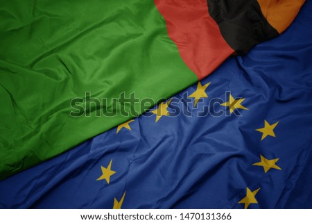 waving colorful flag of european union and flag of zambia. macro