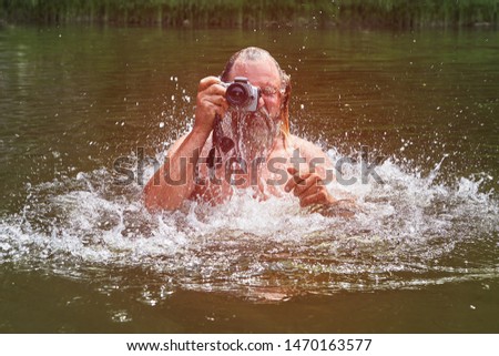 Mature bearded white man is swimming in river and taking photos with waterproof camera, eco-tourism.