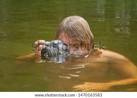 Mature white man is taking photos being in river, his waterproof camera is half in water, eco tourism.