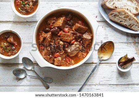 Beef Stew with prunes and vegetables in a pot with bread on a wooden rustic table Royalty-Free Stock Photo #1470163841