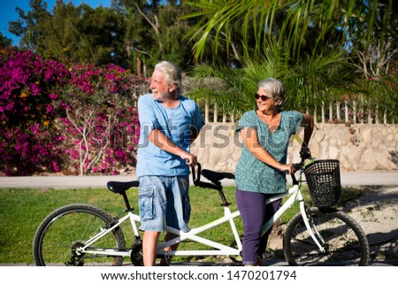 beautiful couple of senior and mature married, riding a doble bike, tandem, together to have fun with a great and sunny day - woman and man - standing looking at the back