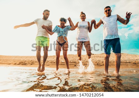 Adorable young friends group have fun and celebrate while jumping and running on the beach