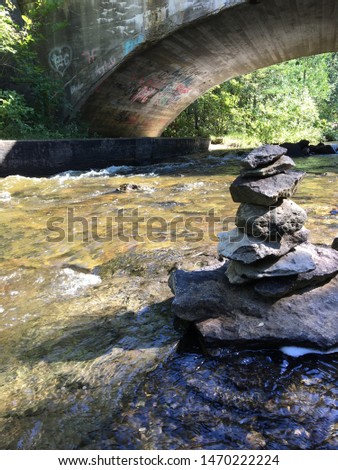 A small rock stack rests on the edge of a river. An old stone bridge in the background looms over the stack.
