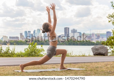 Yoga wellness class outside in city park woman doing high lunge crescent pose on exercise mat outdoors against skyline river view.