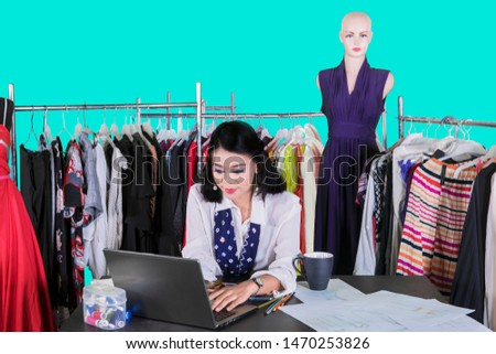 Picture of a female fashion designer typing on a laptop computer while working in the studio