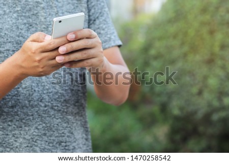 Human hand hold and use smartphone in public park with copy space