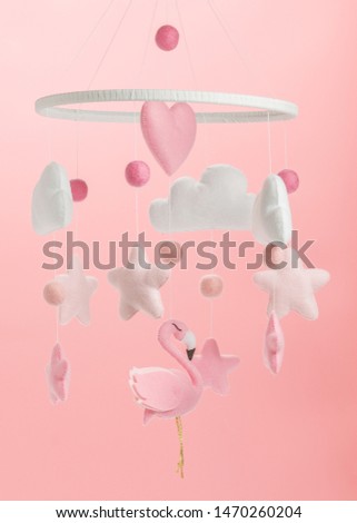 Colorful and eco-friendly children's mobile from felt for children. It consists of flamingo toys, clouds, stars and balloons. Handmade on pink background.