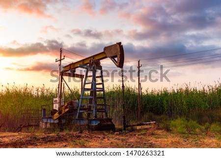 Oil rig pump against a colorful sunset sky