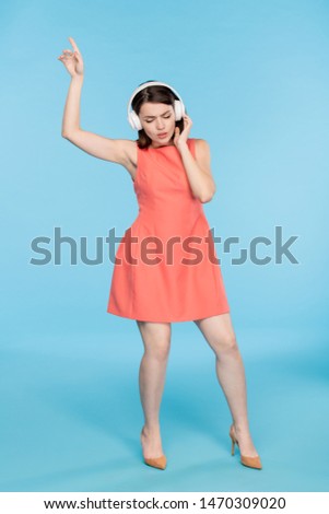 Young elegant woman in red dres enjoying music in headphones while dancing
