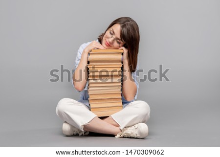 Clever female stuudent with crossed legs keeping her head on top of books