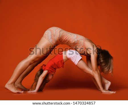 Young mother and 5-year-old daughter doing pilates yoga stretching exercises in a fitness studio on a red background