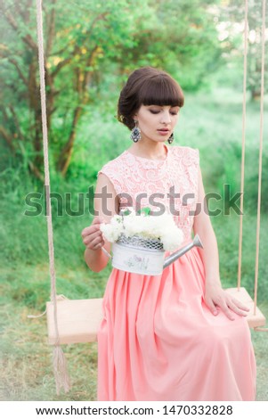 Young attractive girl in a long dress with white flowers in her hands in a summer park at sunset
