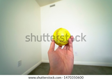 Close up of a hand holding a baseball with white wall in the background