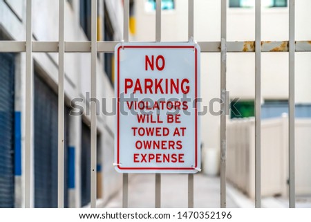 Close up of No Parking sign on awhite metal gate with building in the background