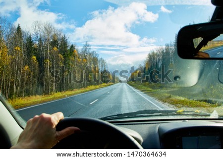 Track from the car window and white clouds on blue sky. Natural landscape during travel in auto. Woman's hand on the steering wheel. Female driver seeing beautiful landscape