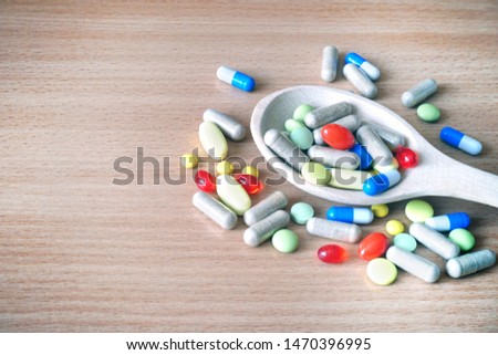 medicine pills, tablets and capsules in wooden spoon on wooden background with copy space