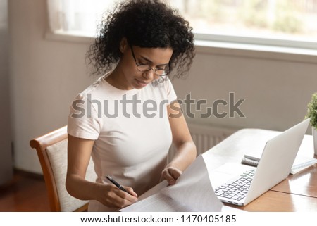 Concentrated young african american business woman in eyeglasses sitting at table with computer, reading terms of condition, preparing business contract, signing documents, medical insurance. Royalty-Free Stock Photo #1470405185