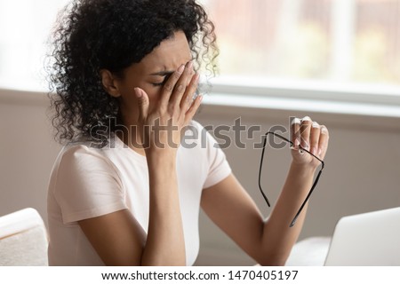 Tired african american millennnial woman dropping eyeglasses, rubbing eyes, feeling exhausted after long working day with computer, suffering from eye strain, blurred vision, dry eyes syndrome. Royalty-Free Stock Photo #1470405197