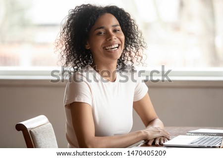 Cheerful funny mixed race young woman sitting at desk, distracted from job, looking aside, talking with somebody, having fun during work break, joking, laughing, relaxing, feeling positive at home. Royalty-Free Stock Photo #1470405209