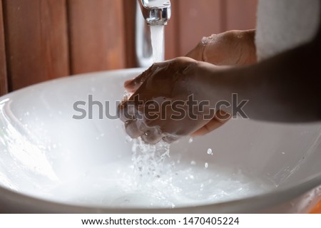 Close up cropped image young african ethnicity guy washing hands under running water in modern sink. Black guy gathering water in hands to wash face. Morning personal hygiene routine, water overuse.
