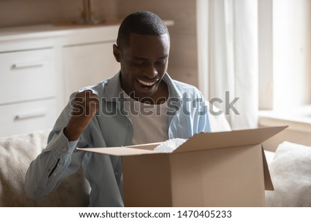 Excited african ethnicity happy smiling guy holding opened carton box, satisfied with fast easy delivery service from online internet store. Positive customer getting ordered items safe and sound. Royalty-Free Stock Photo #1470405233