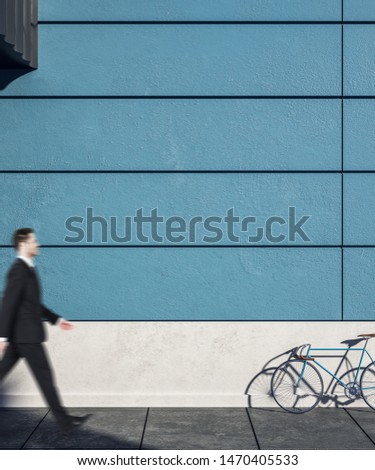 Businessman walking past empty blue exterior wall with bicycle on street, empty copyspace and sunlight. Mock  up,