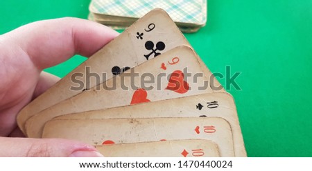 set of playing cards of different suits in female hand over deck of cards laying on green table