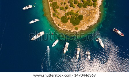 Anchored yachts surrounding an island with turquoise waters in the Agean sea