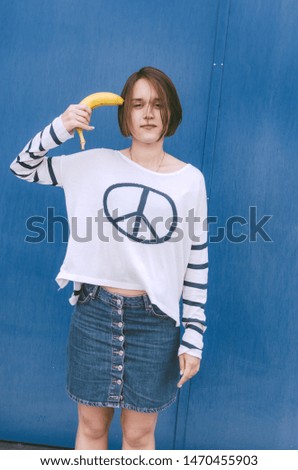 Young adult female staying with banana on blue wall