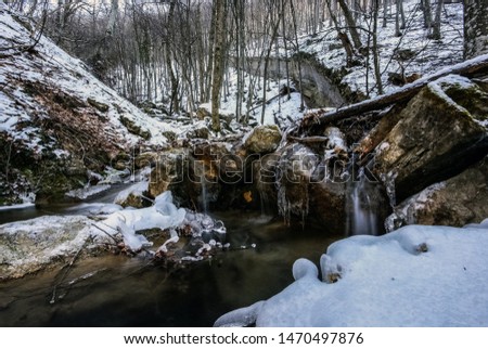 A cold, babbling stream of blue tinted melt water flows after a winter snowstorm. Cascading mountain stream through snow covered woods.Stream in the winter forest. Fairy winter forest with a stream