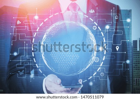 Businessman looking at smartphone in city with double exposure of global business hologram. Concept of hi tech and communication. Toned image