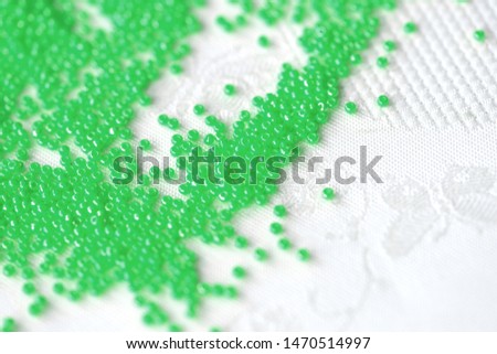 Seed beads green color scattered on a white textile background close up