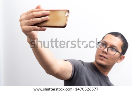 The skin head man in the grey t shirt is holding the smart phone in the right hand and taking the selfie isolated on white background, casual, technology, minimal, hipster concept.