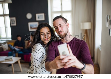 A group of young friends with smartphone indoors, taking selfie.