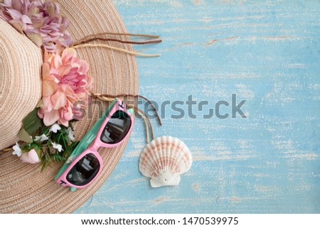 Concept of travel on the beach. Women hat, pink sunglasses and seashell. Blue wooden background.