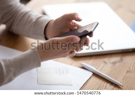 Close up young woman hands holding smartphone on table with notes. Distracted from work female student sitting at desk, studying, reading email or typing message for friends, shopping, web surfing.