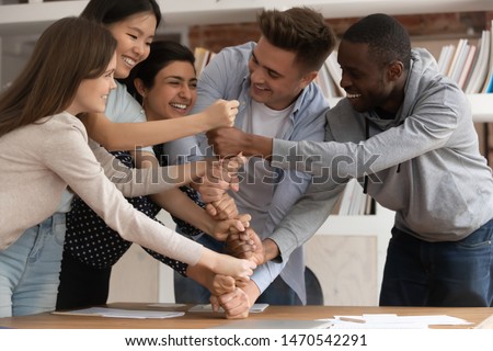 Overjoyed mixed race young students involved in funny game or teambuilding activity, making fists pyramid. Happy smiling diverse young people demonstrating multiracial unity, support and cooperation. Royalty-Free Stock Photo #1470542291